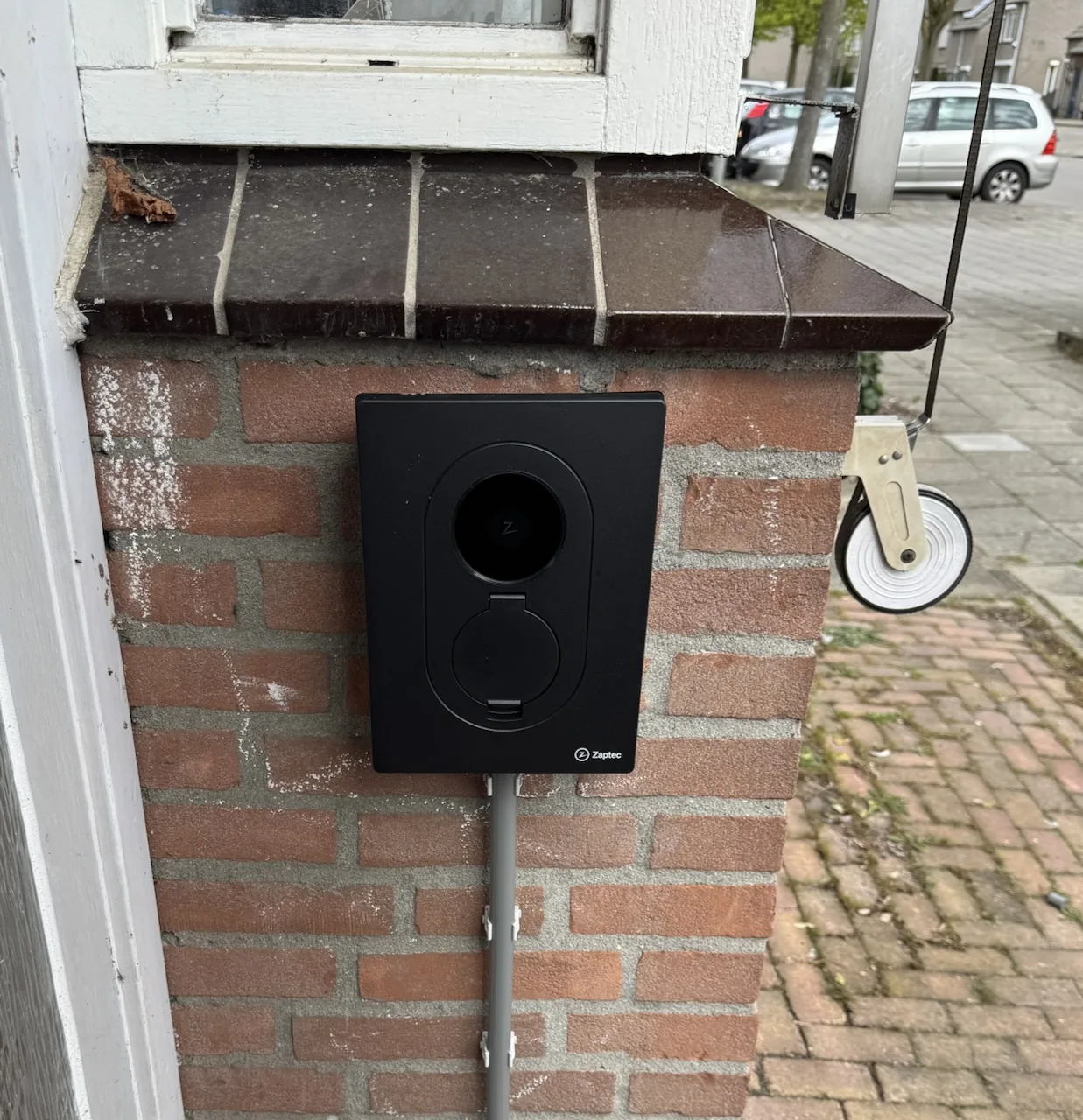 Black Zaptec Go 2 EV charger mounted on a brick exterior wall in Geldrop